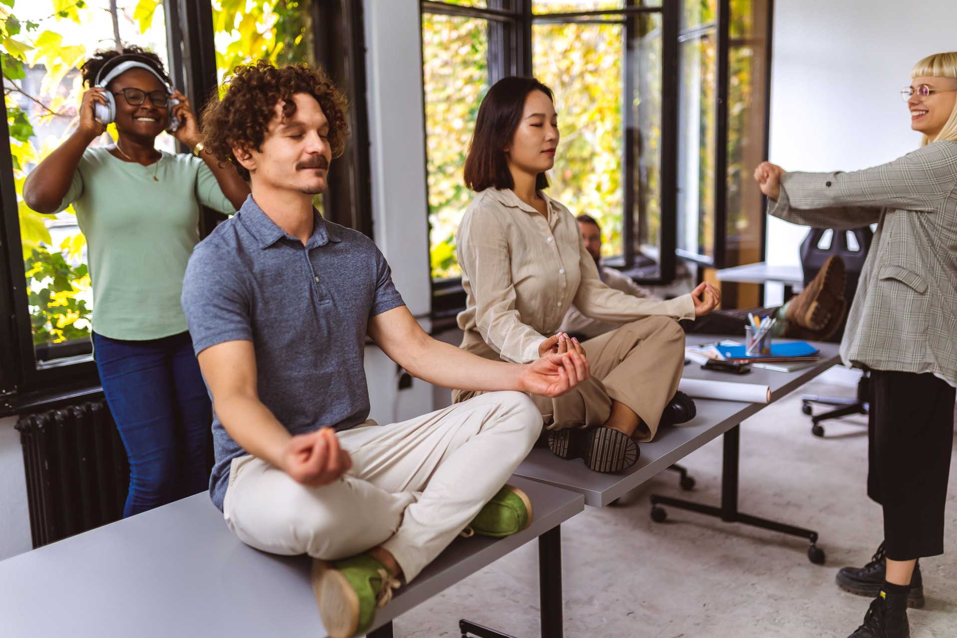 Young business people doing relaxation exercises at casual office. Meditation in office. People listening to the music in the background.